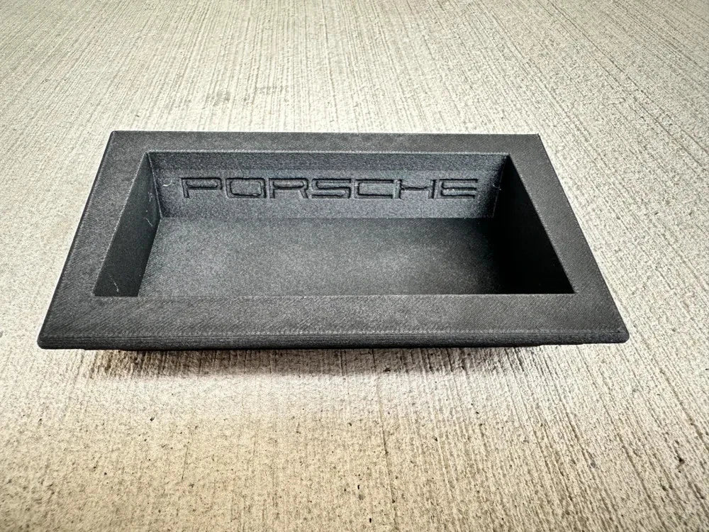 Black rectangular object with 'Porsche' branding on a textured surface